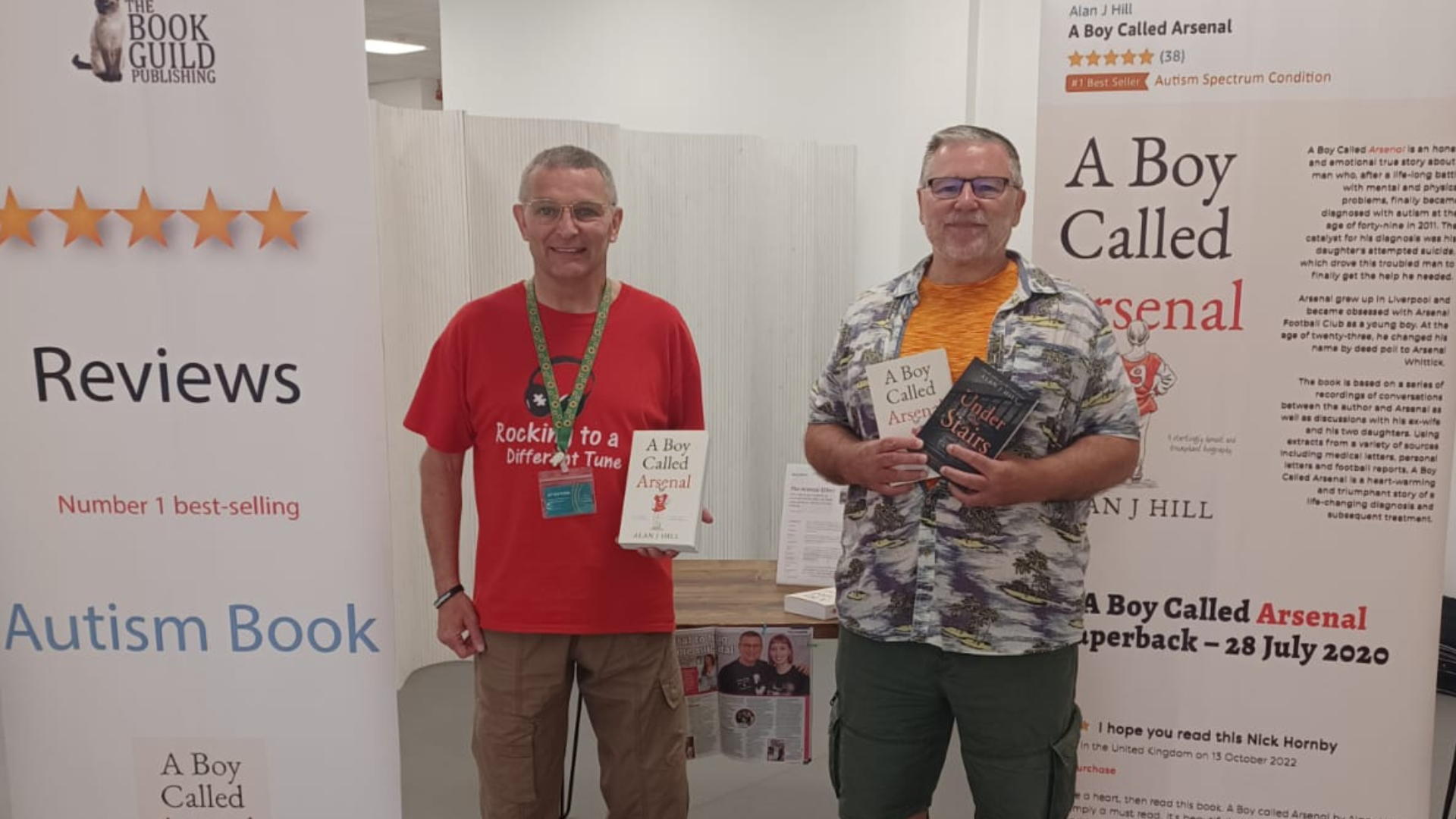 Arsenal Whittick (left) and Alan J Hill (right) holding copies of A Boy Called Arsenal, and standing in front of banners promoting the book. One of the banners reads, 'number-one best-selling Autism book.'